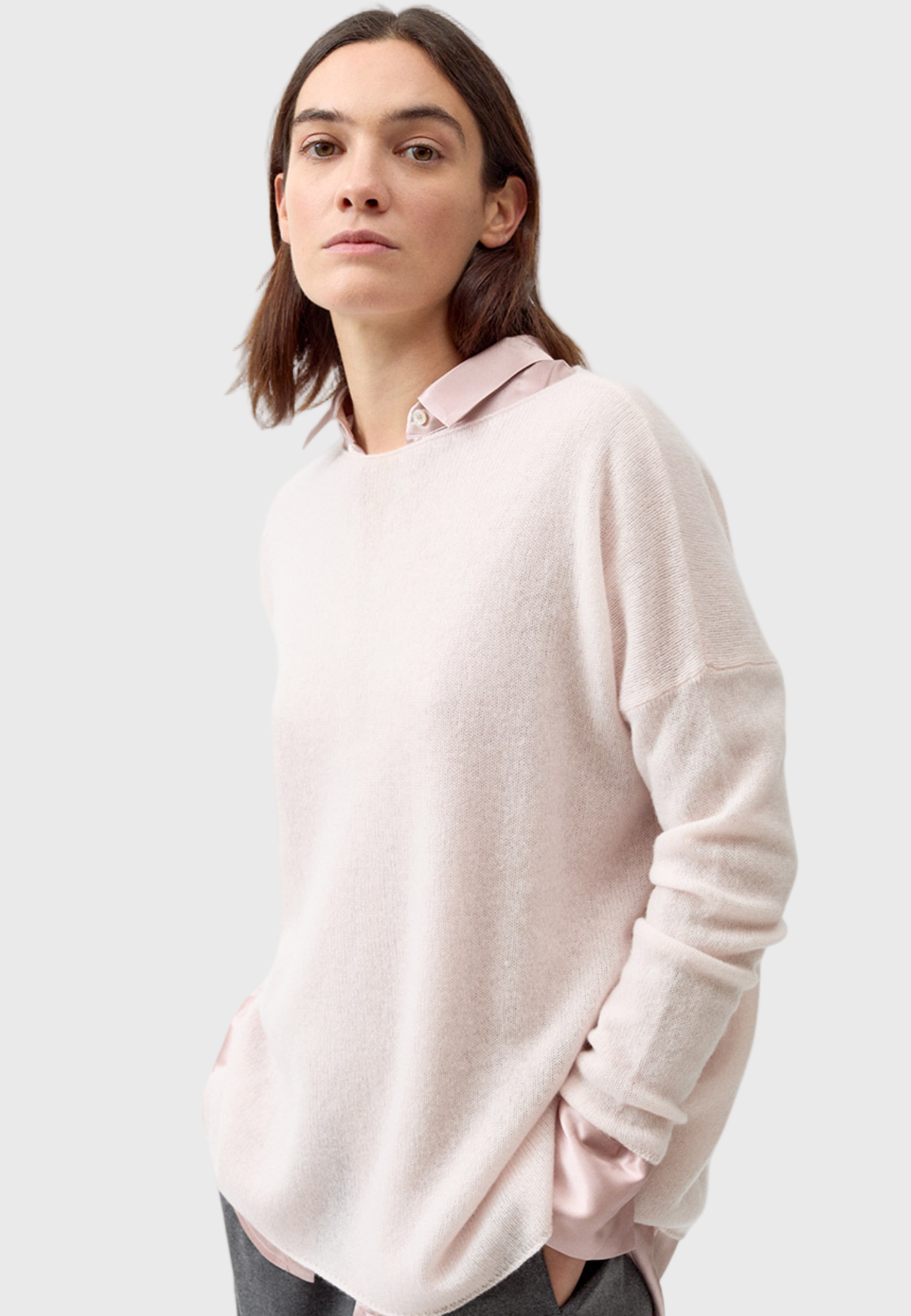 A woman wearing a light pink, slightly oversized cashmere sweater with long sleeves.