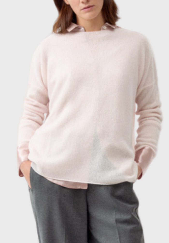 Woman wearing a light pink sweater and gray pants on a white background