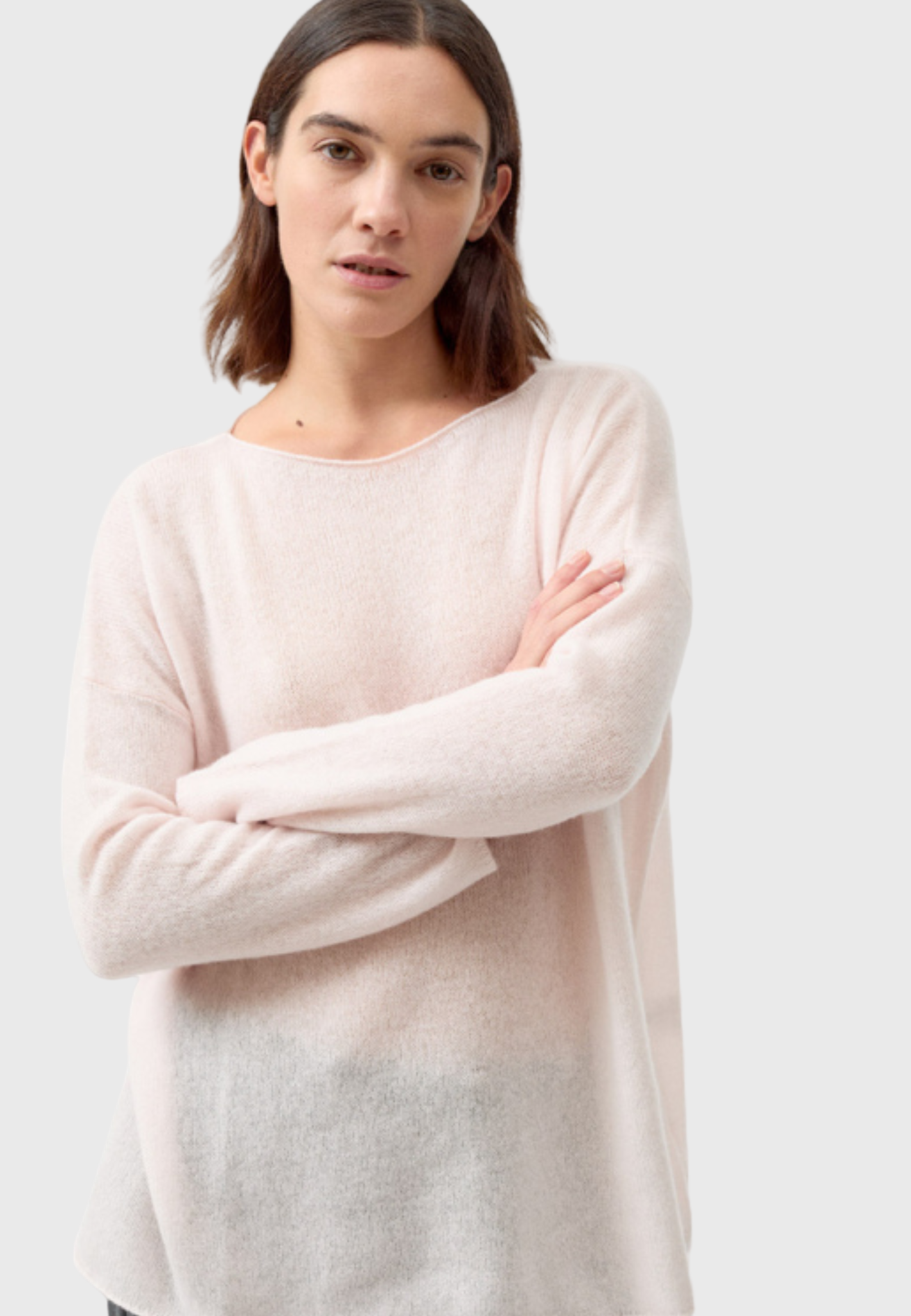 Woman wearing a light pink sweater and gray pants on a white background