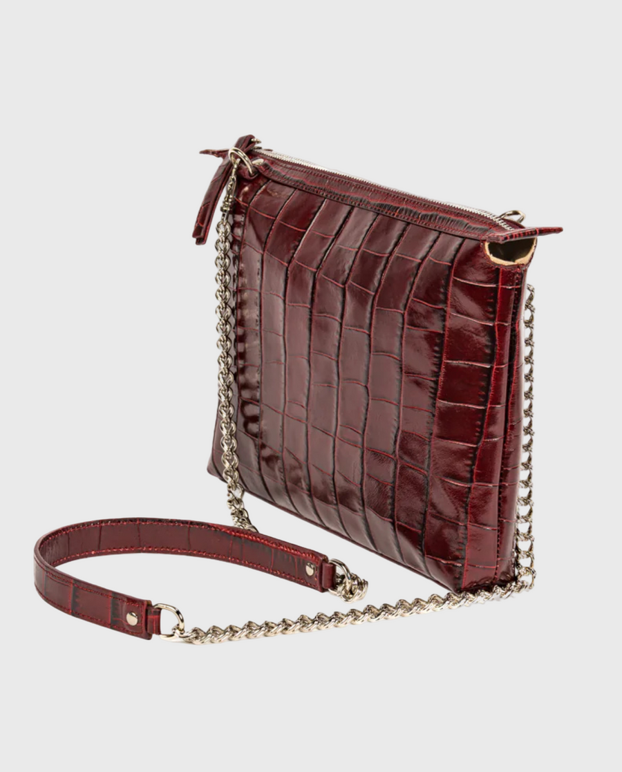 A burgundy croc-embossed leather crossbody bag with a chain strap and a zip closure, displayed against a neutral background.