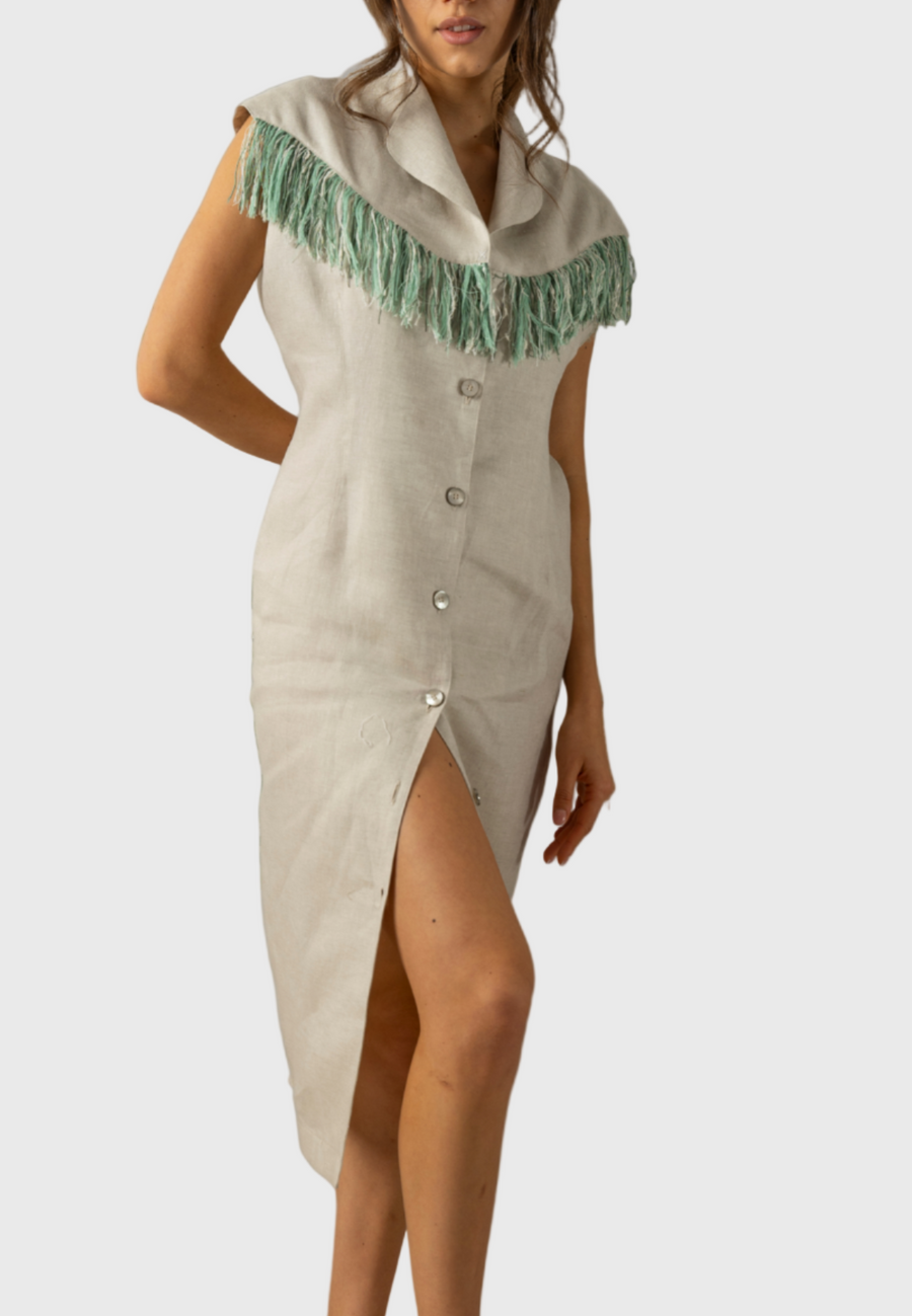 A model wearing a beige knee-length A-line dress with earthy green fringed details on the sleeves and a double-breasted design.