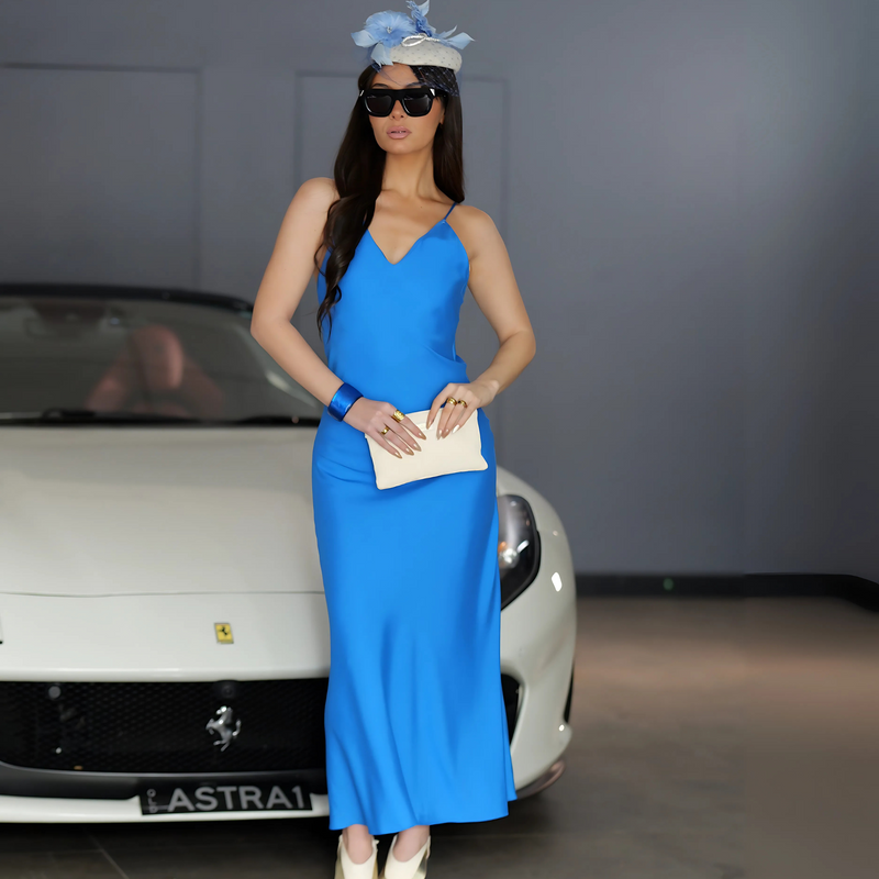 Woman in a blue dress and hat standing in front of a Ferrai  white car with a visible brand logo.