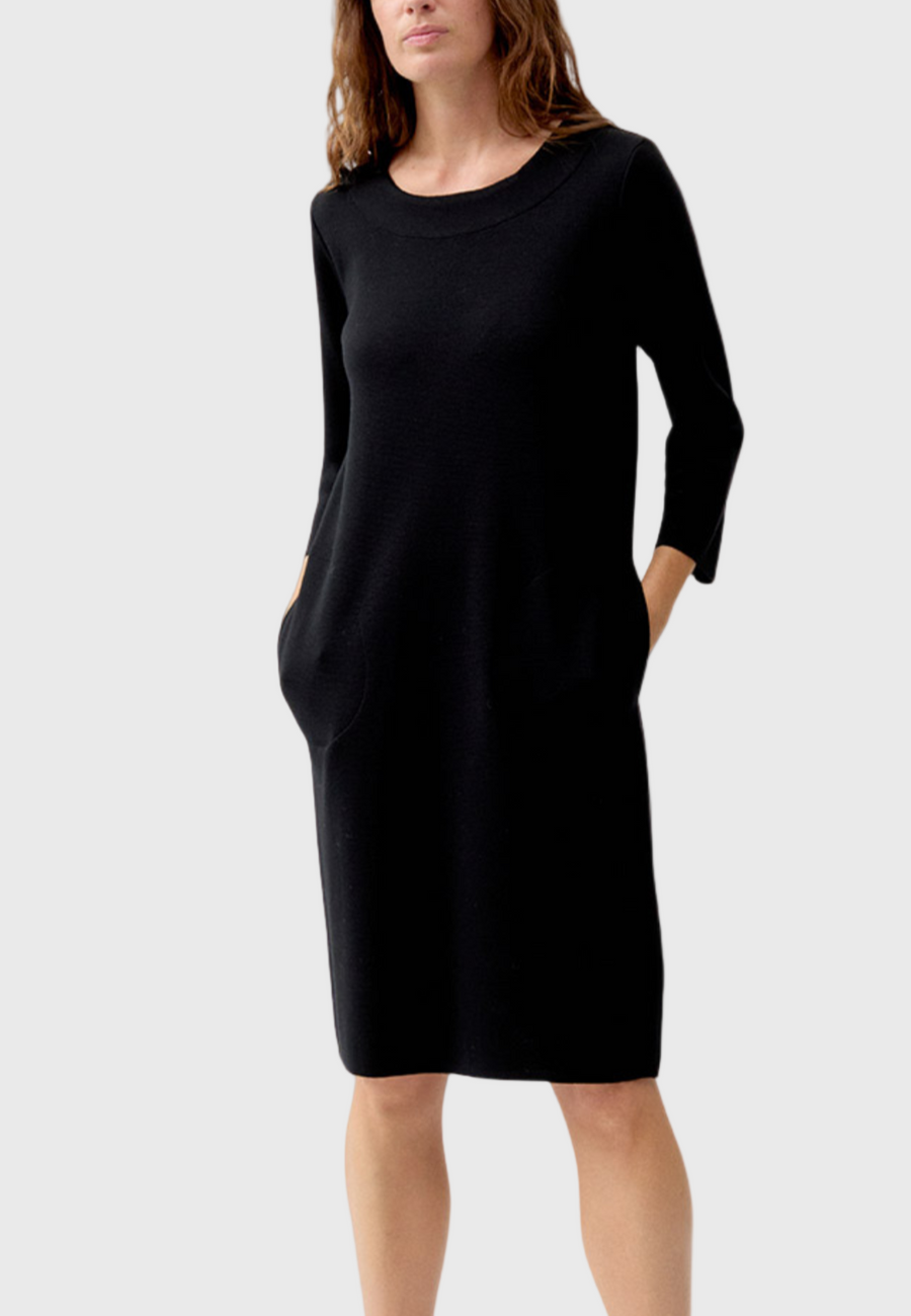 A model wearing a straight black dress with a round neckline, three-quarter sleeves, and a knee-length cut.