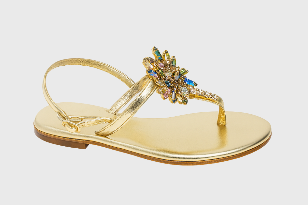 Gold sandal with a decorative embellishment on a light gray background