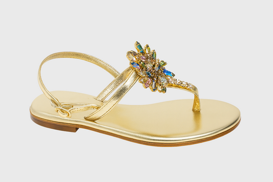 Gold sandal with a decorative embellishment on a light gray background
